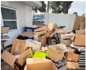 Commercial junk removal project - pile of cardboard boxes and trash scattered in a paved area outside a white building