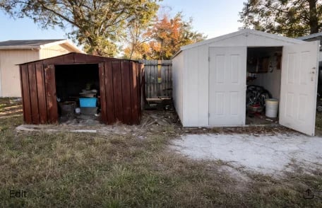Two storage sheds in a backyard with autumn trees, one brown and one white, both with open doors
