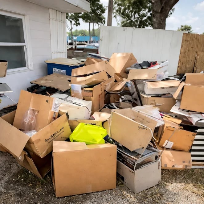 Large pile of cardboard boxes and assorted items stacked in a residential outdoor area near a white building