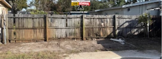 Shed removal site - wooden fence with metal posts in a dirt lot next to a building with a yellow sign