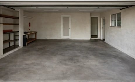 Empty garage interior with concrete floor, white walls, shelving unit, and overhead door