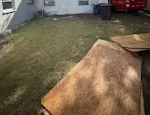 Carpet removal project - rolled up carpet laid on grass outside house with red truck in background