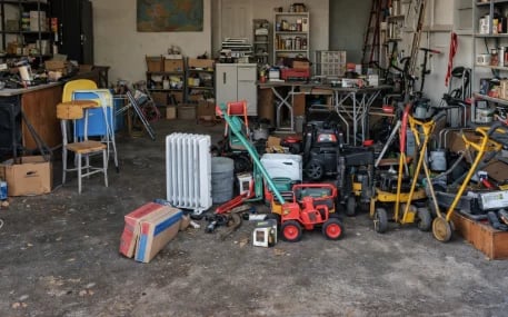 Crowded garage workshop filled with various tools, equipment, hand trucks, and storage items organized throughout the space