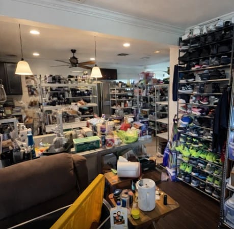 Cluttered hobby room with shelves of collectibles, work desk, pendant lights, and gaming memorabilia displayed throughout